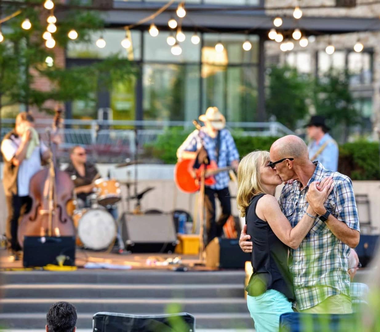 Couple kissing and dancing in front of live music with a stage and band in the background.