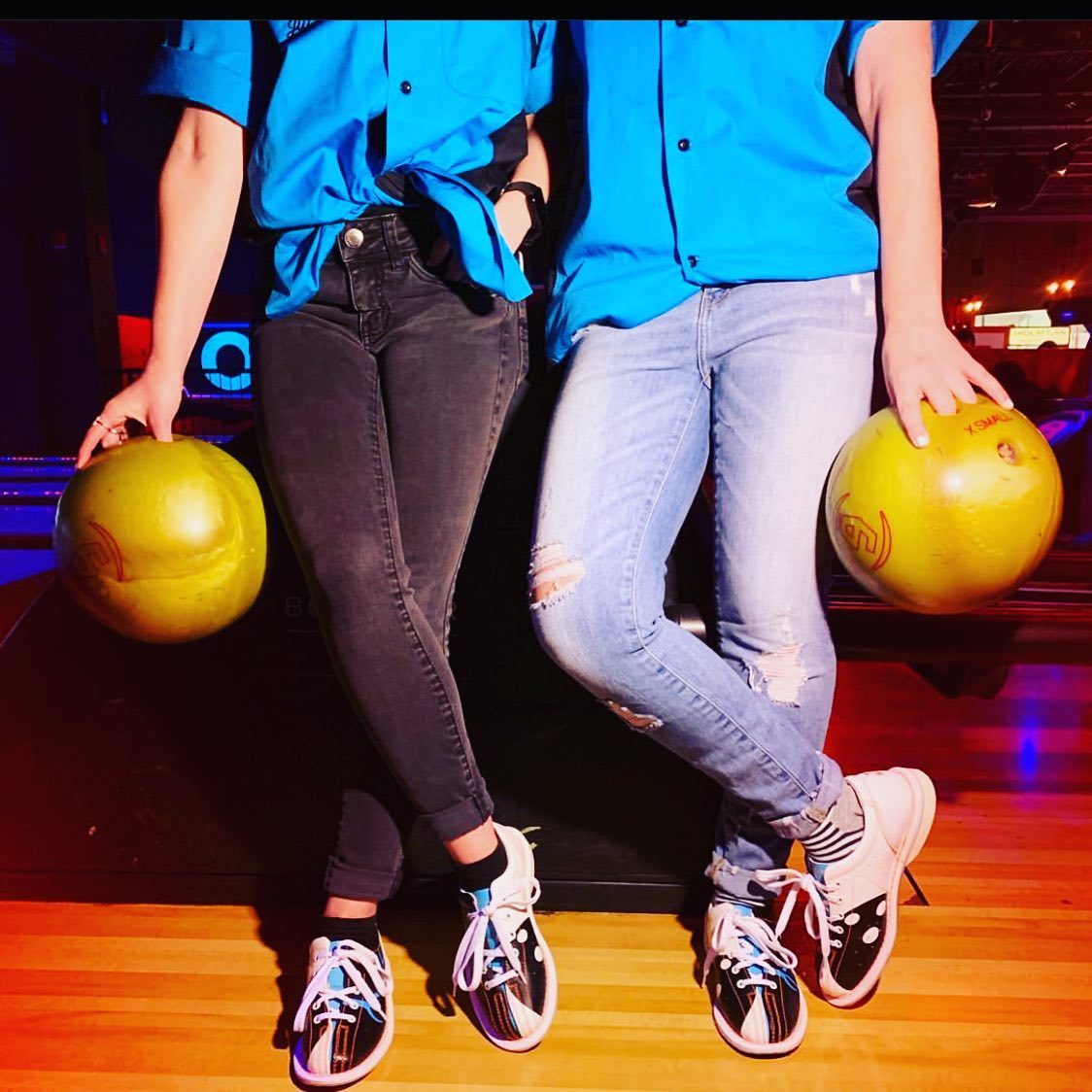 Two people wearing bowling shoes and holding bowling balls