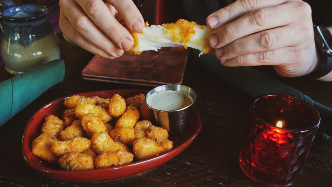 Plate full of deep-fried cheese curds with hands pulling one apart.