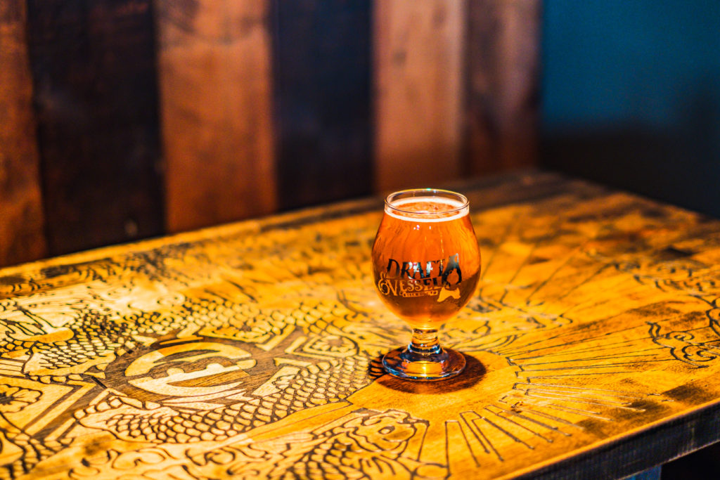 Cup of Draft and Vessel beer on carved wooden table.